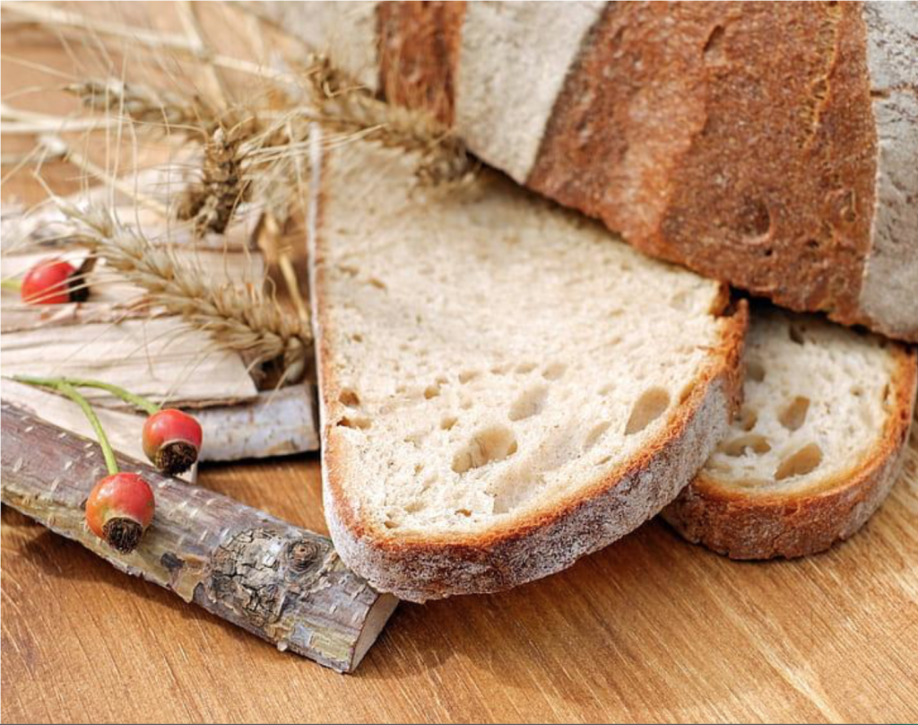View of freshly baked bread and wheat arranged on a rustic wooden table.